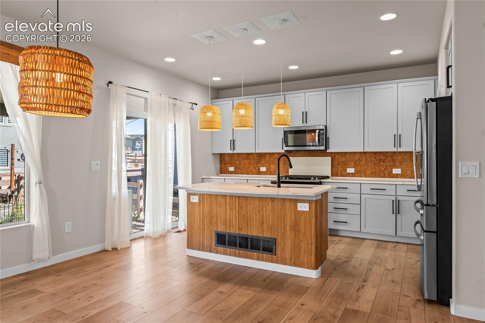 Kitchen featuring light-gray shaker-style cabinetry, wood-finish flooring, a kitchen island with a natural wood-tone base, stone-texture backsplash, and stainless-steel appliances