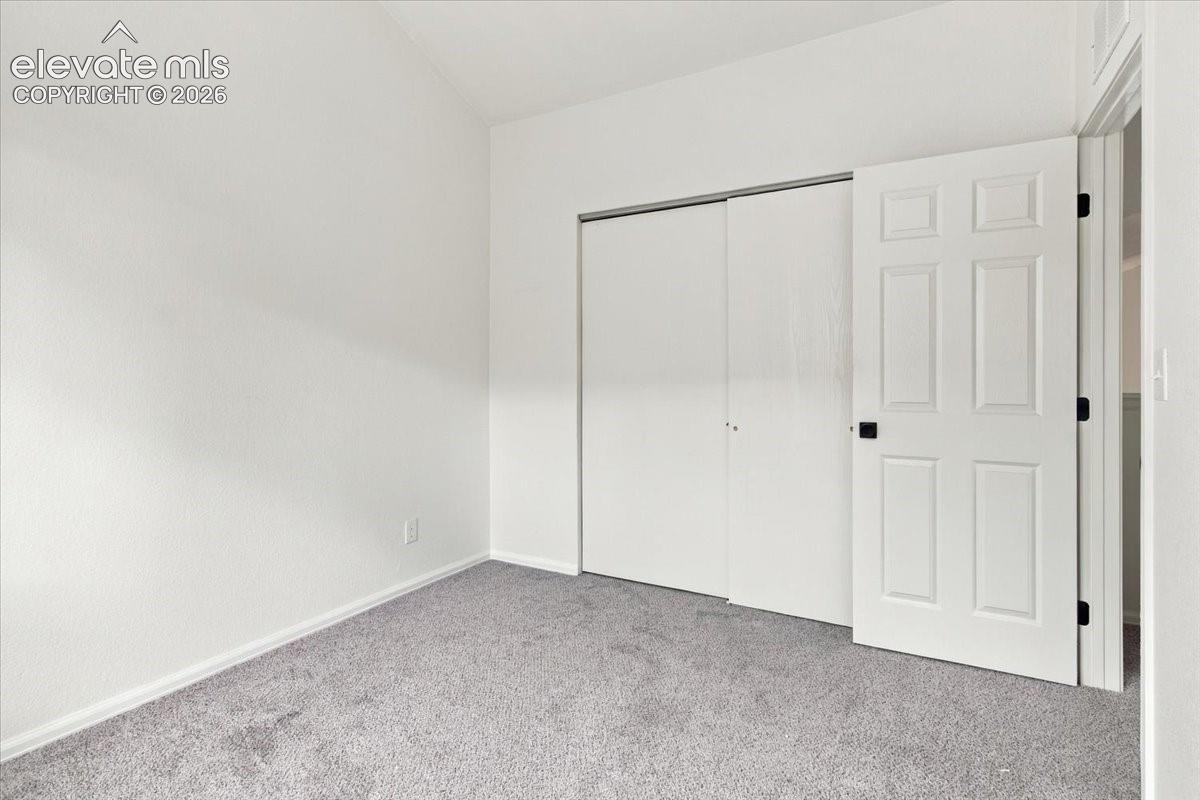 Room featuring vaulted ceilings, neutral carpeting, a six-panel interior door, and a sliding door closet