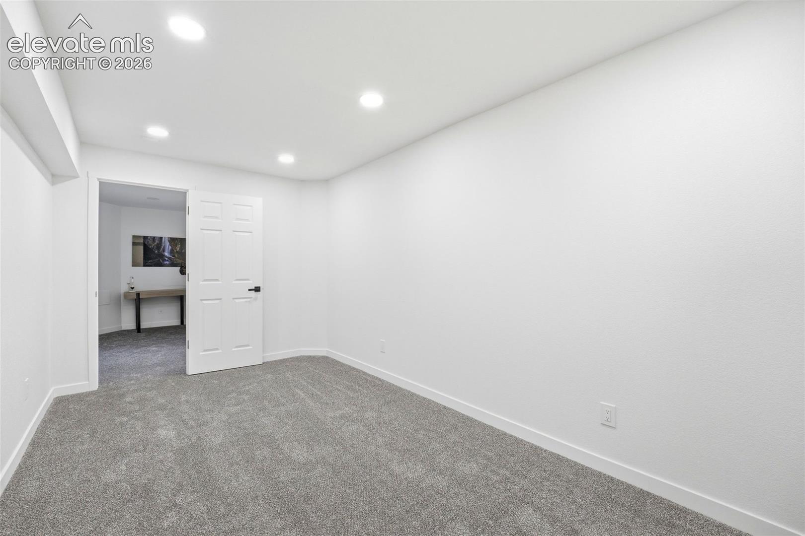 Spacious room with new gray carpeting, crisp white walls, and recessed lighting