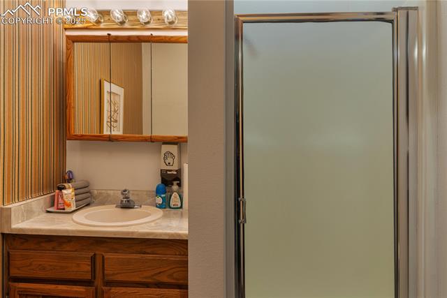 Full bath featuring vanity, a shower stall, and wallpapered walls
