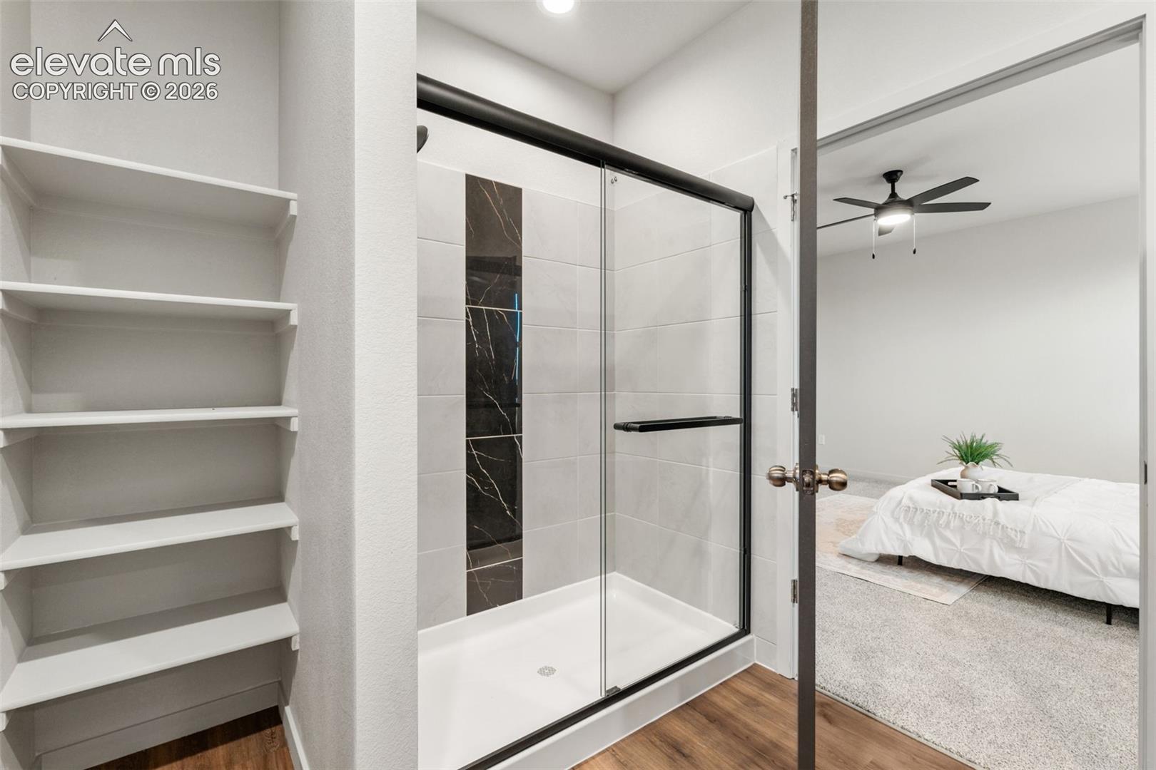 Shower stall featuring a glass enclosure with black framing, integrated shelving, and large-format tile surround with a decorative vertical accent strip