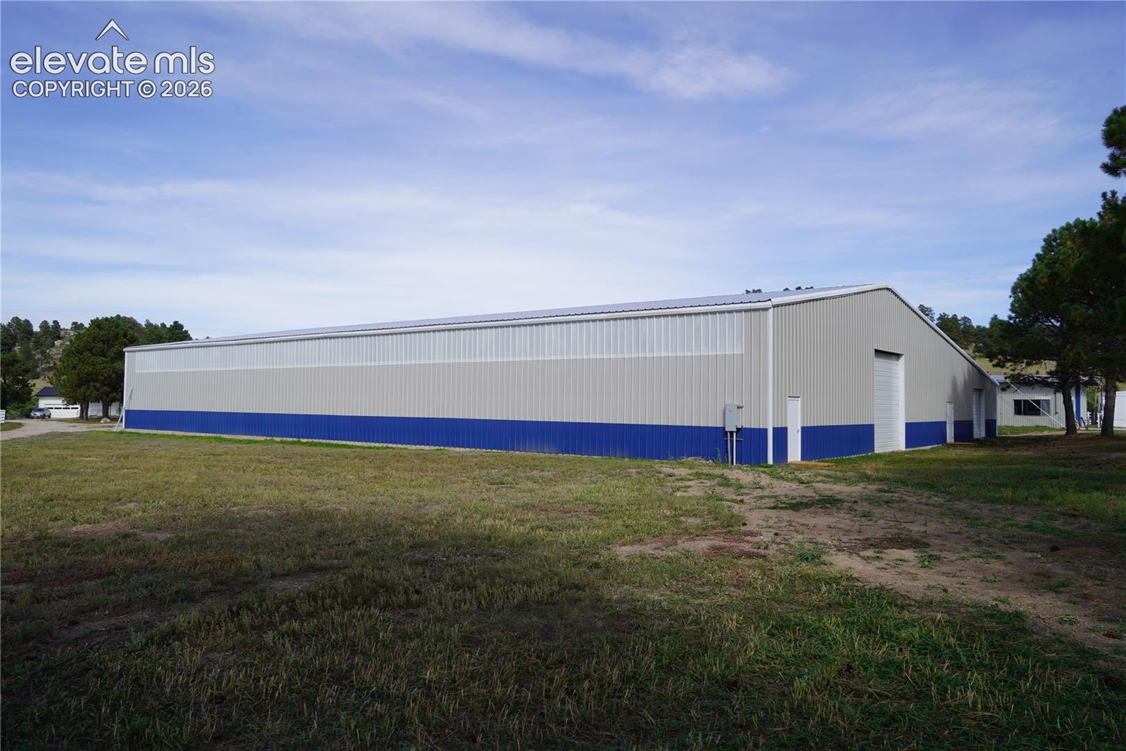 Arena - Expansive metal building featuring a pitched roof, multiple entry doors, a large roll-up door, and a two-tone exterior