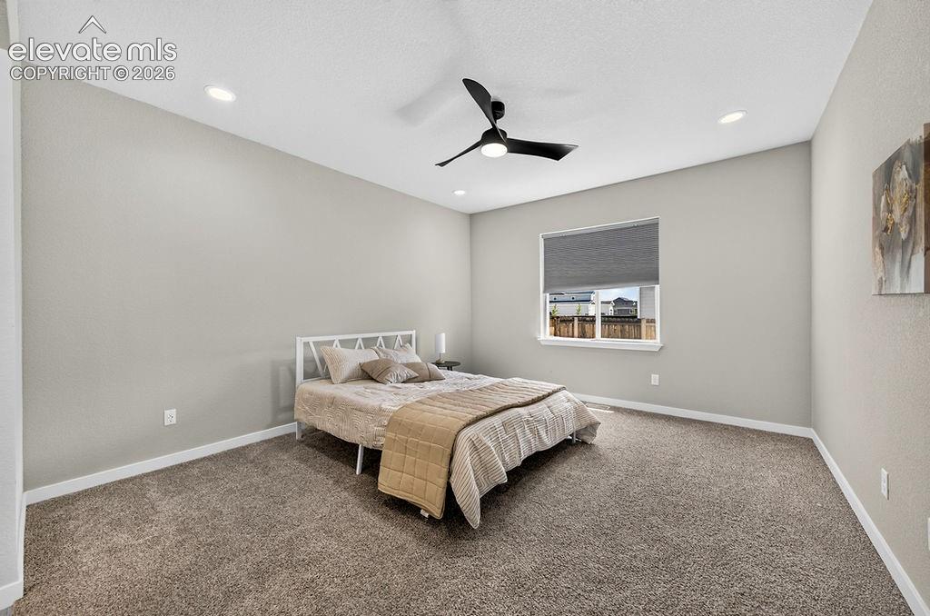 Carpeted room featuring a modern ceiling fan, recessed lighting, neutral wall tones, a window with roller shade, and white baseboards