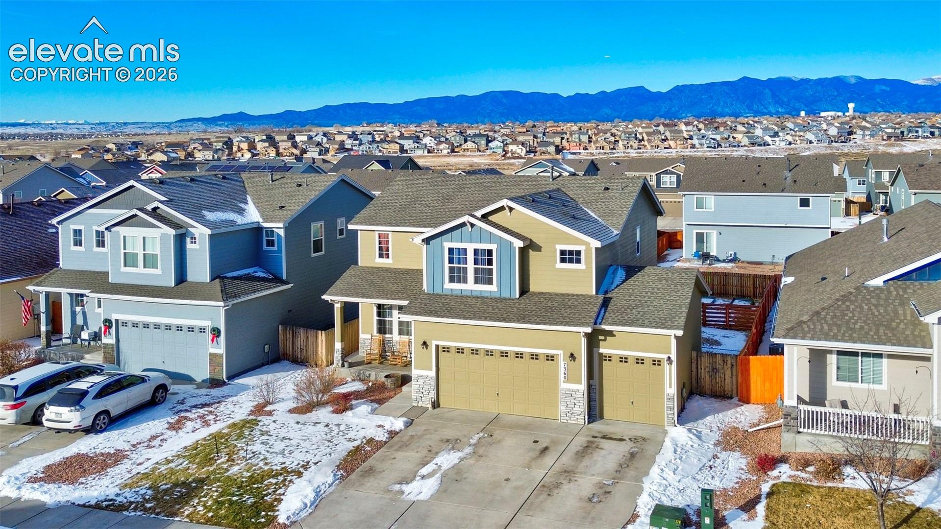Two-story residence featuring multi-tone siding, a three-car garage, stone veneer accents, and mountain backdrops