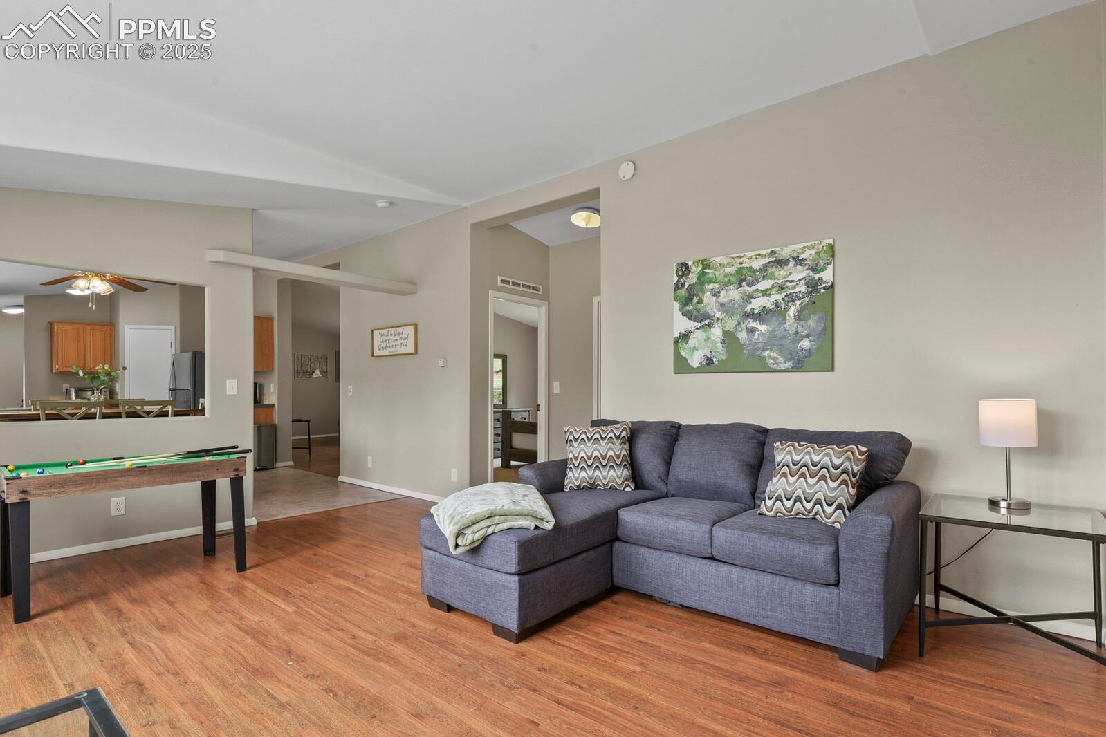 Living room with light wood finished floors, a ceiling fan, and vaulted ceiling