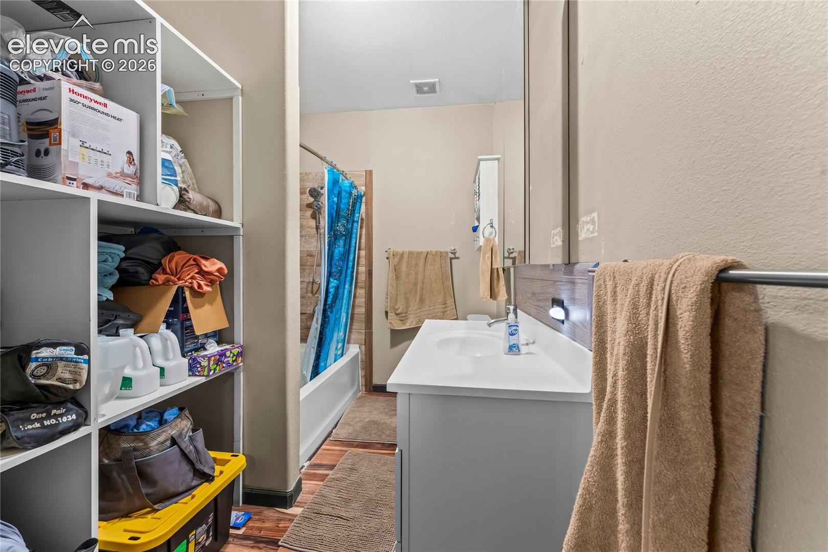 Bathroom featuring a white cabinet vanity with a solid surface countertop, wood-finish flooring, built-in shelving unit, and a tiled shower surround