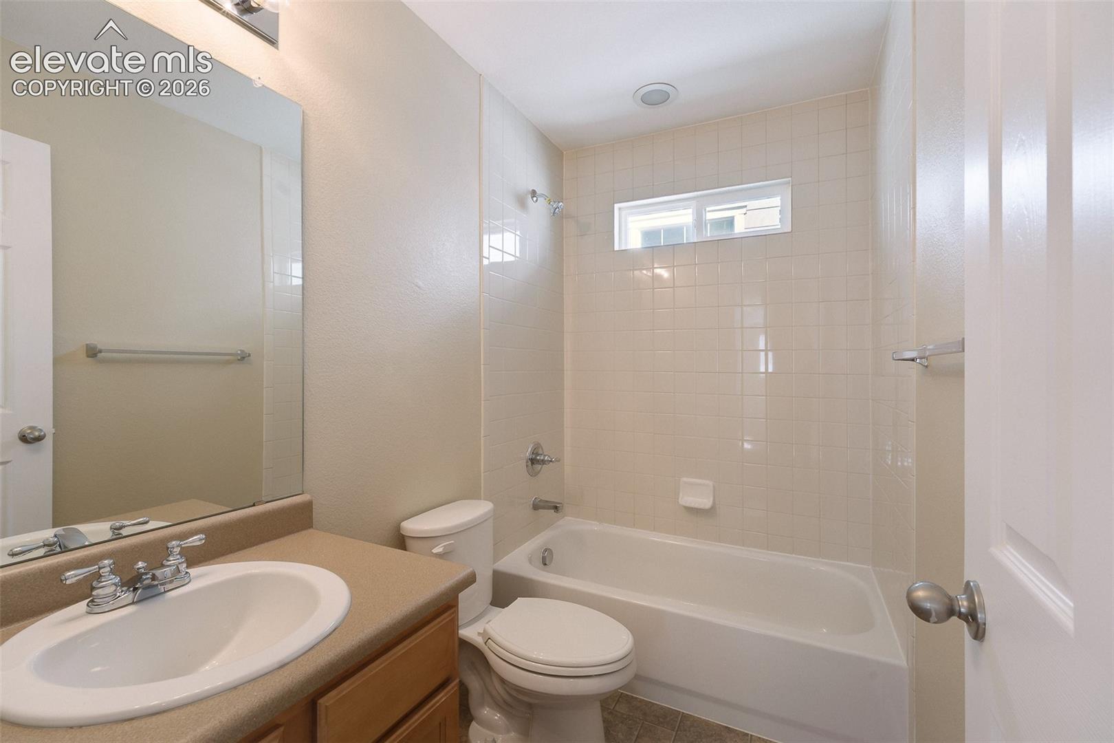 Full bathroom featuring a tub-shower combination with tile surround, vanity with an integrated sink, large wall-mounted mirror, and horizontal window