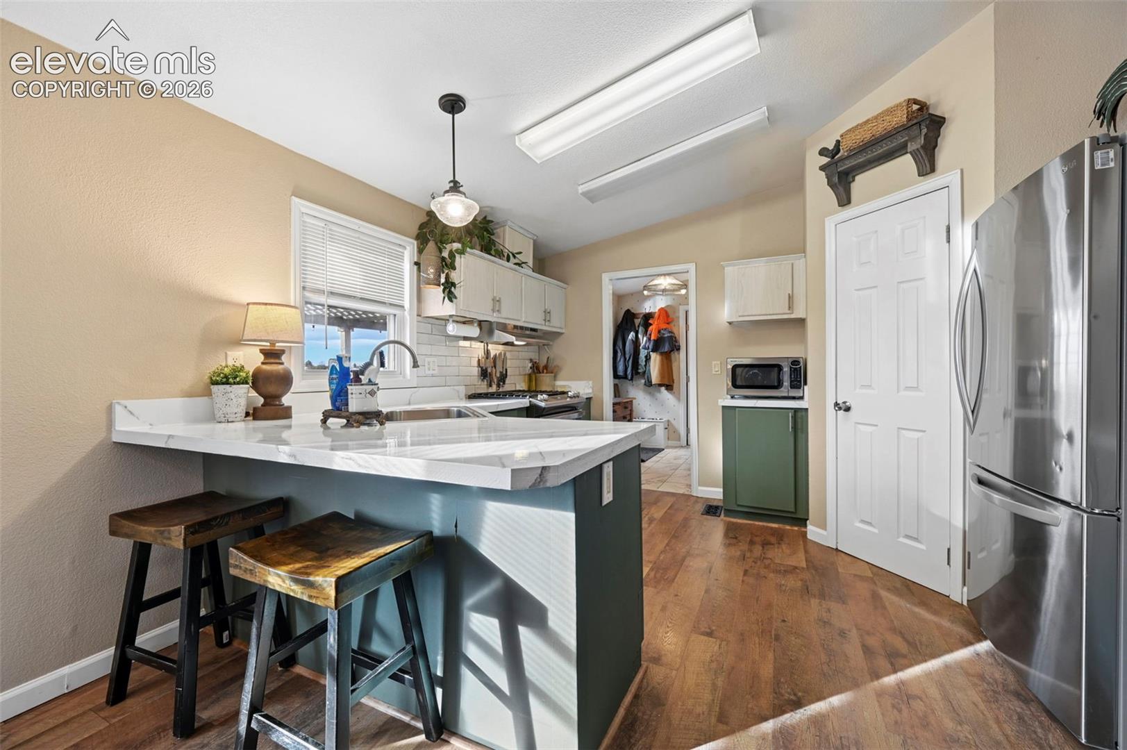 Kitchen featuring wood-finish flooring, stone-surfaced island countertop, stainless steel refrigerator, white cabinetry, and a subway tile backsplash