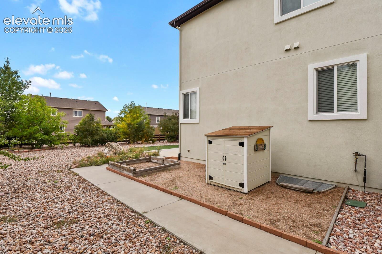 Expansive exterior with stucco siding and multiple windows, featuring a gravel ground cover and concrete pathway
