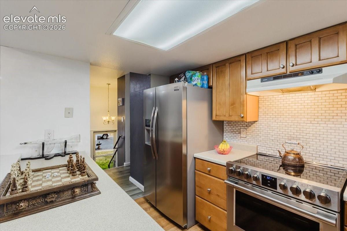 Kitchen featuring stainless steel appliances, wood-finish cabinetry, light-toned countertops, and a white subway tile backsplash