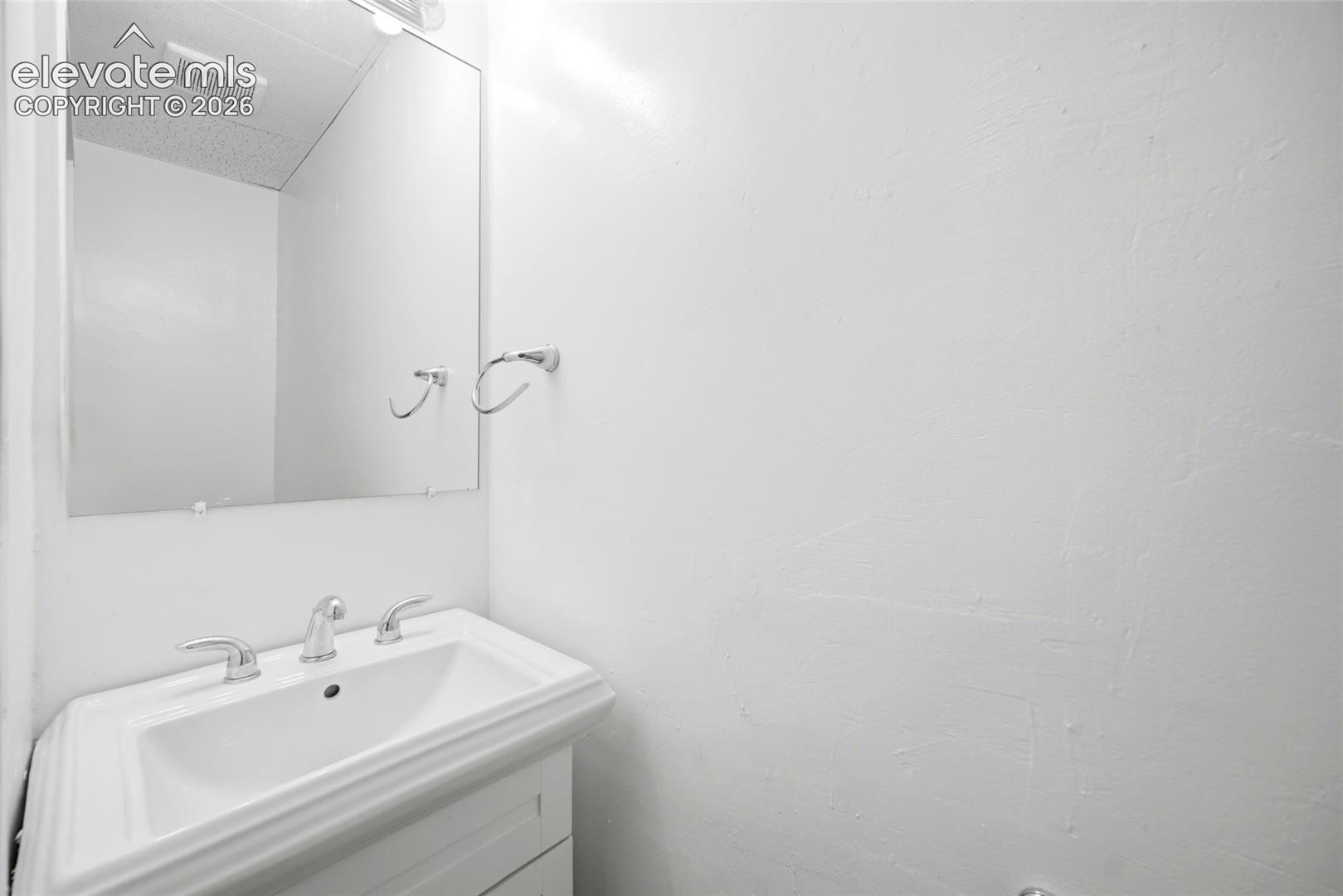 Wall-mounted rectangular mirror, white vanity cabinet with a integrated sink, and polished chrome widespread faucet