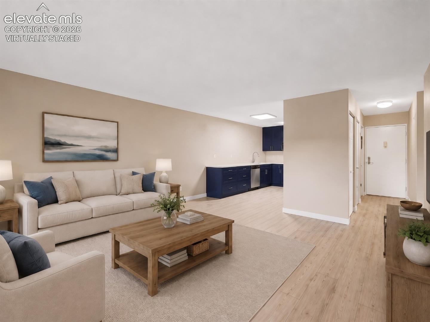 virtually staged Open-concept living space featuring wood-finish flooring, neutral wall tones, and a functional wet bar with navy cabinetry and a stainless steel sink
