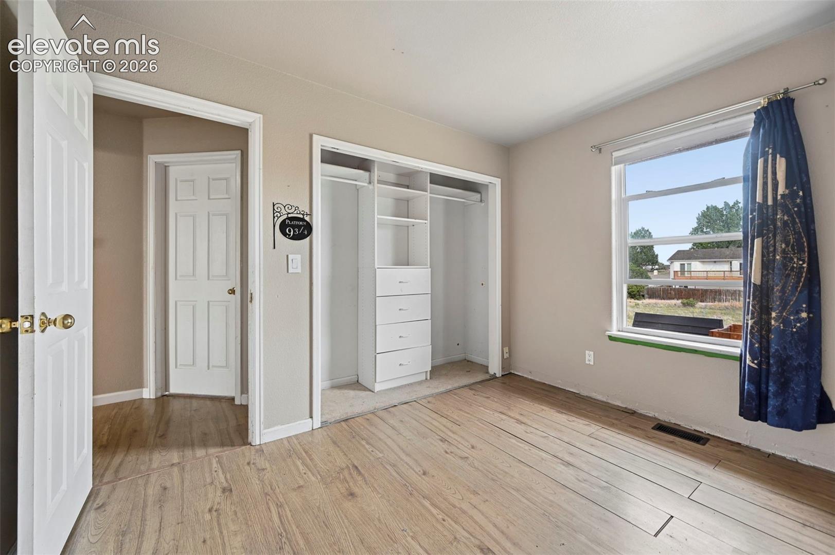 Room featuring wood-finish flooring, neutral wall paint, and a built-in closet system with shelving and drawers