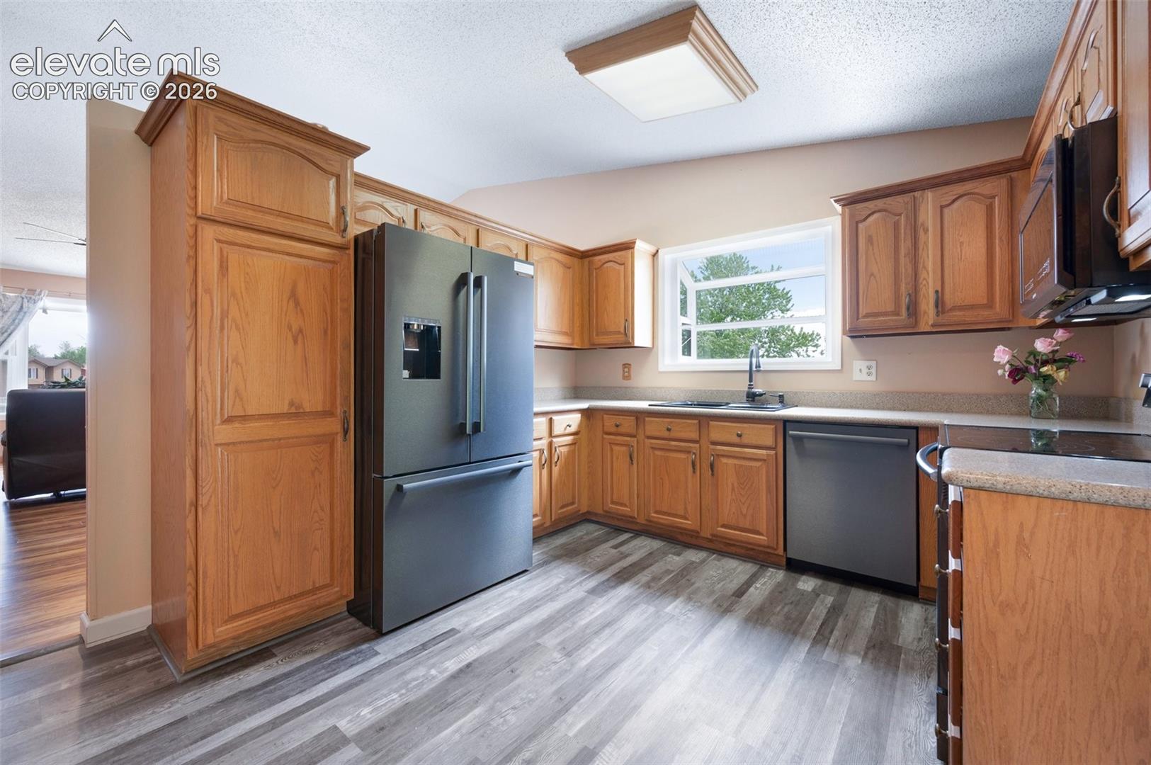 Kitchen featuring appliances with stainless steel finishes, a sink, light wood-style floors, brown cabinets, and light countertops
