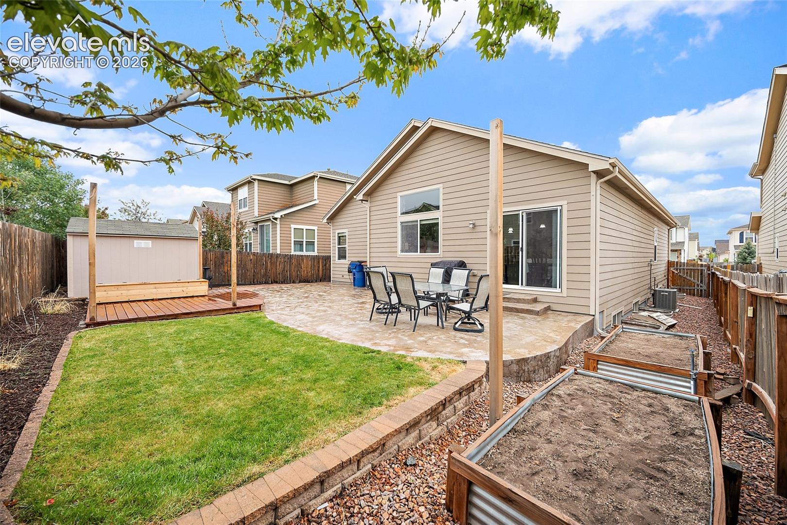 Landscaped backyard with lawn space, raised garden beds, and a large stamped concrete patio.