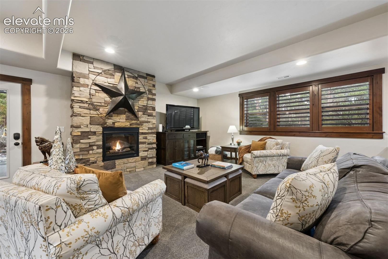 Floor-to-ceiling stone fireplace, recessed lighting, and large windows featuring dark wood-finish trim and plantation-style shutters