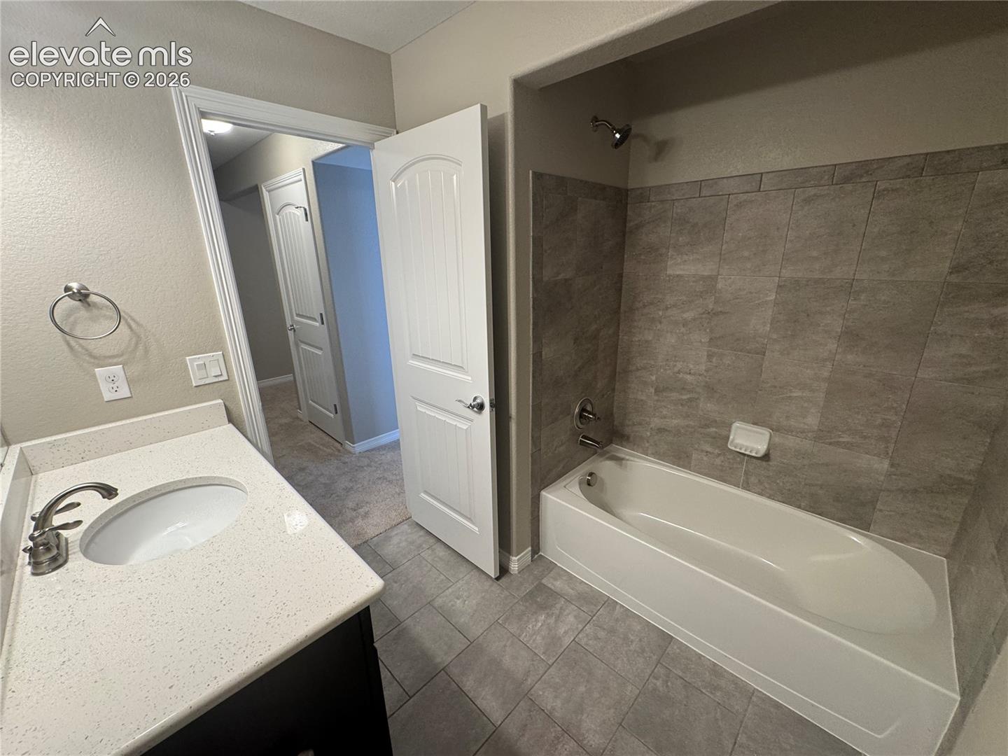 Bathroom featuring a vanity with a light-toned solid surface countertop, tile flooring, and a tub-shower combination with full-height stone-finish wall tile