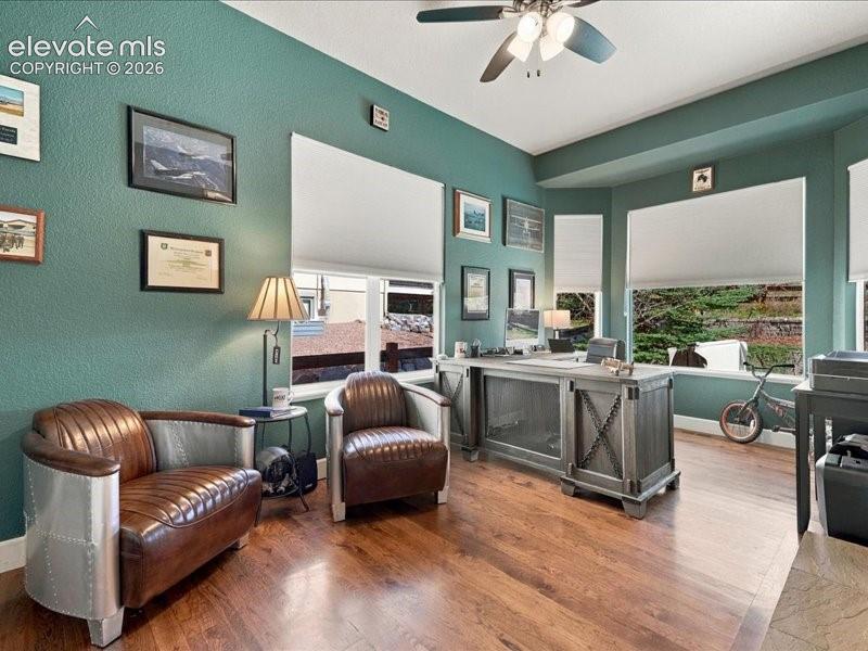 Hardwood-finish flooring, multiple windows with roller shades, and a ceiling fan with integrated lighting