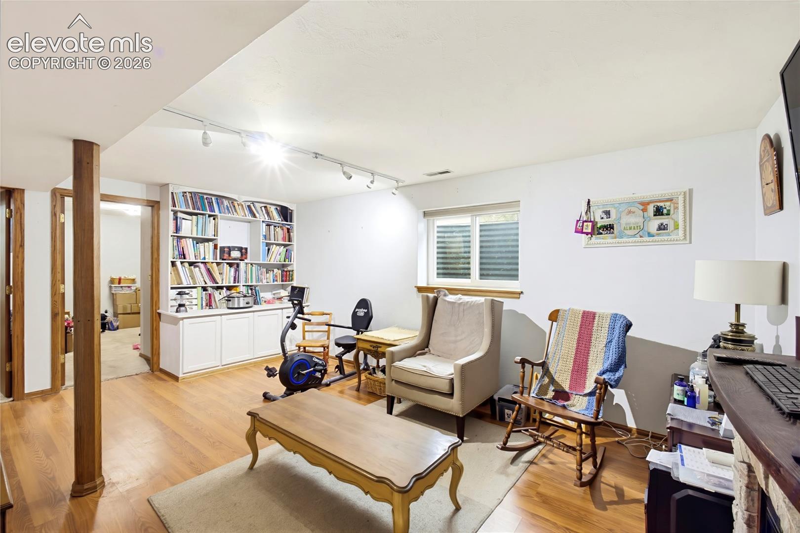 Hardwood-finish flooring, built-in shelving, white cabinetry, track lighting, and a window with blinds