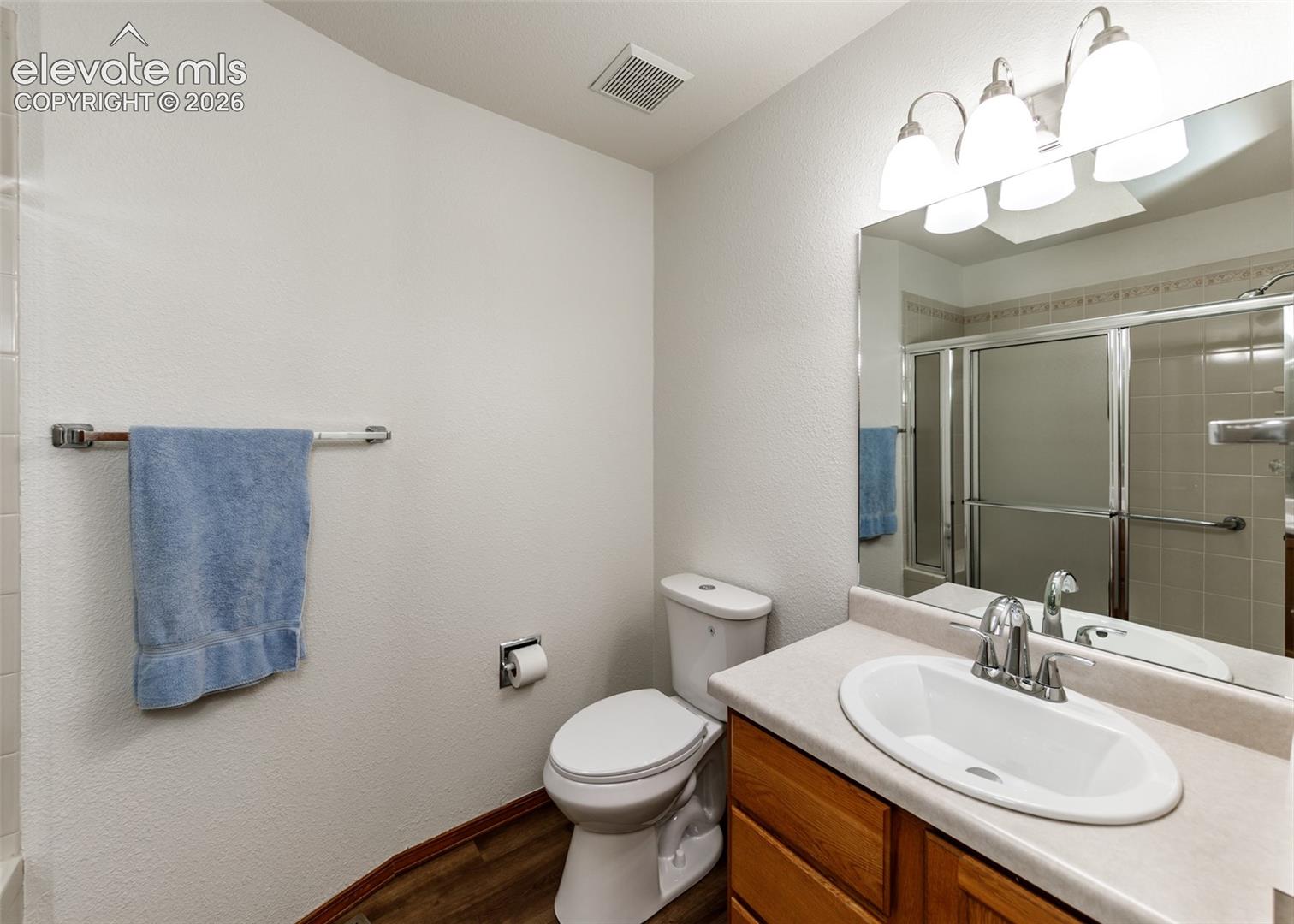 Bathroom with wood-finish flooring, a vanity with wood cabinetry, an oval undermount sink, and a shower with a sliding glass enclosure