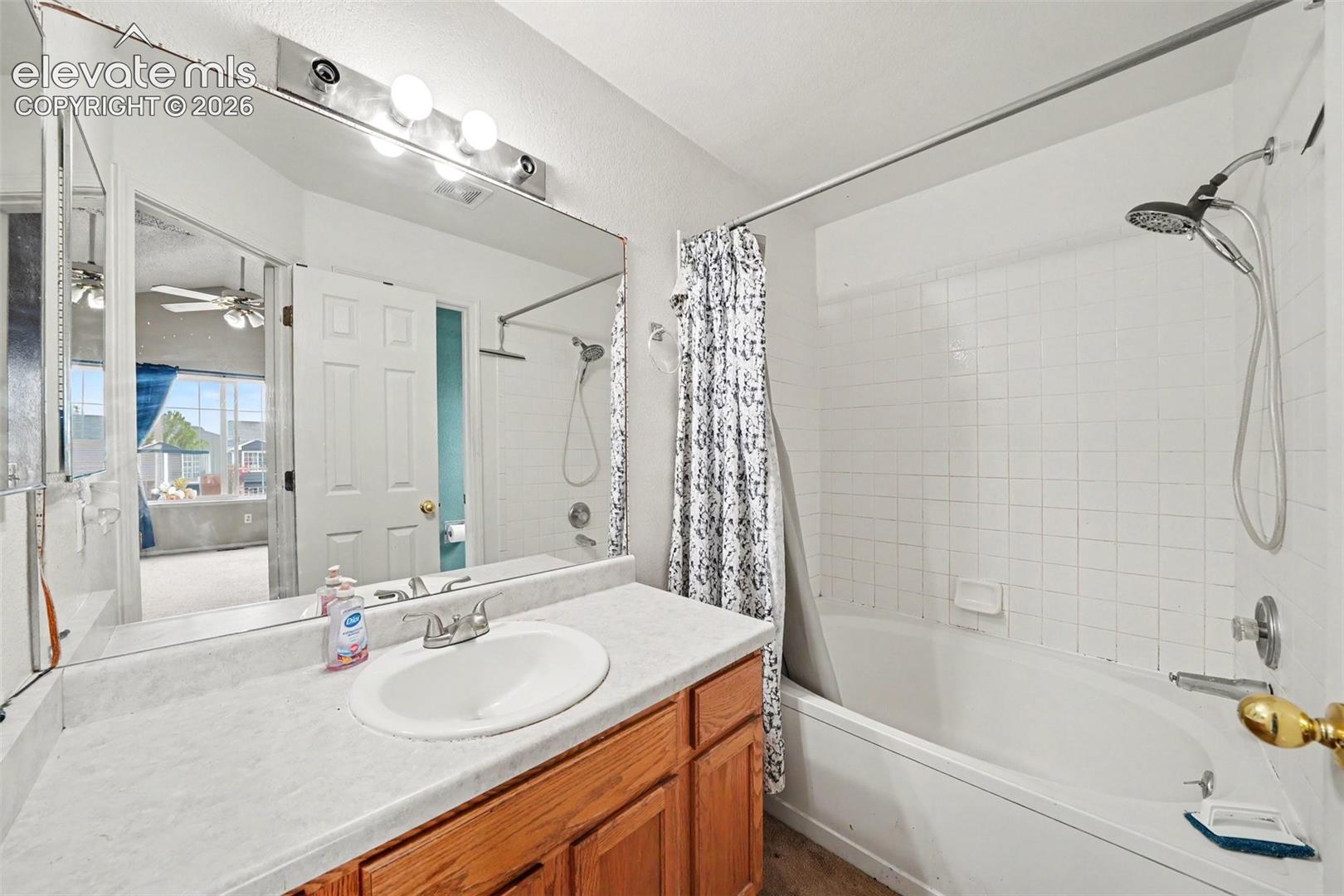 Bathroom featuring a vanity with a white integrated sink, wood-finish cabinetry, a large wall-mounted mirror, a four-bulb light fixture, and a tile-surround shower and tub combination