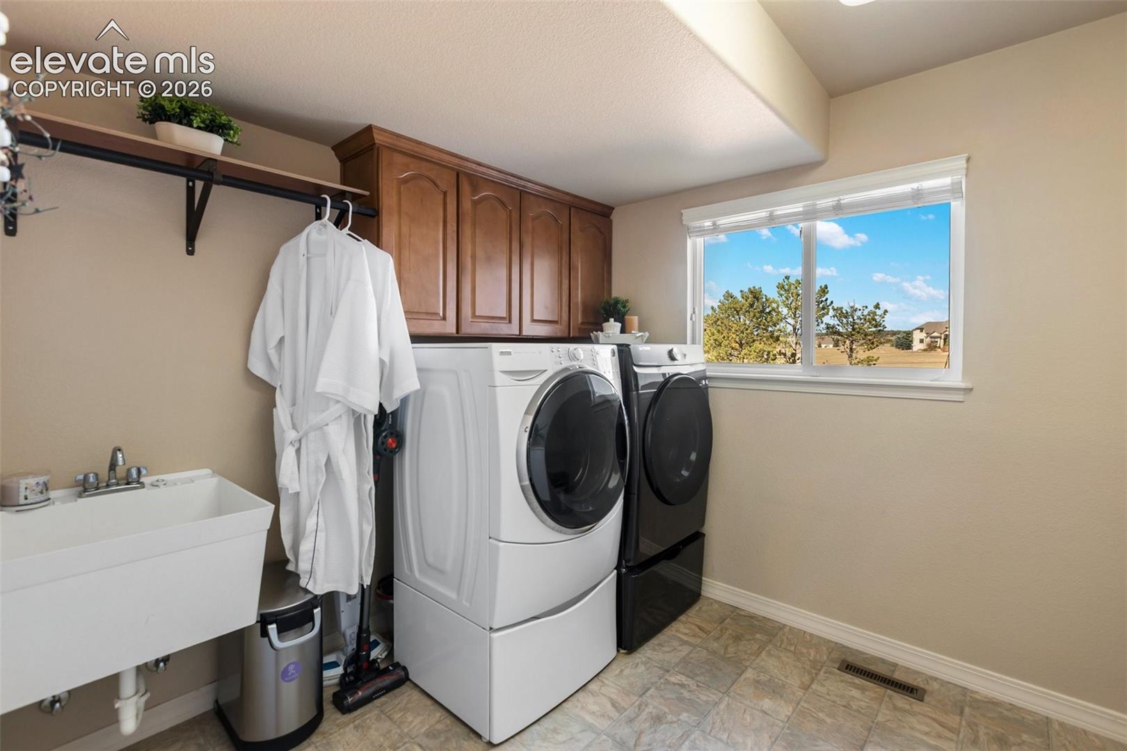 Laundry room featuring wood-finish upper cabinetry, a wall-mounted utility sink with a metal faucet, and tile flooring