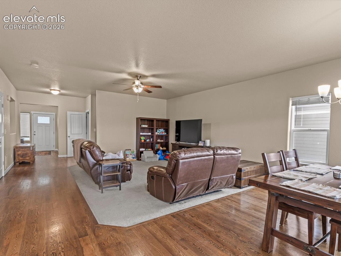 Open-concept living area featuring wood-finish flooring, a ceiling fan, and a dining space with an overhead light fixture