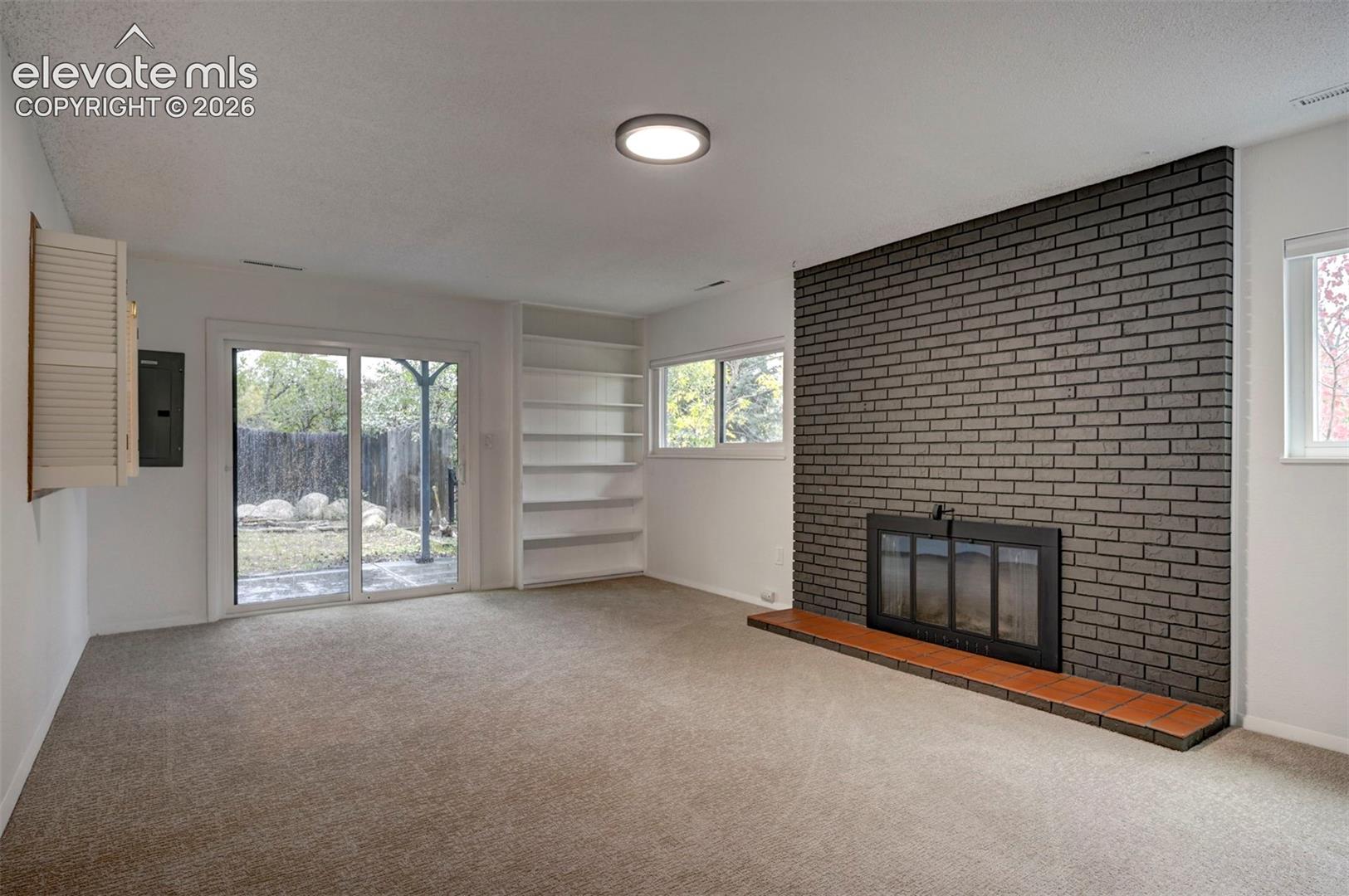 Floor-to-ceiling brick fireplace surround, built-in shelving, sliding glass door, and neutral carpeting
