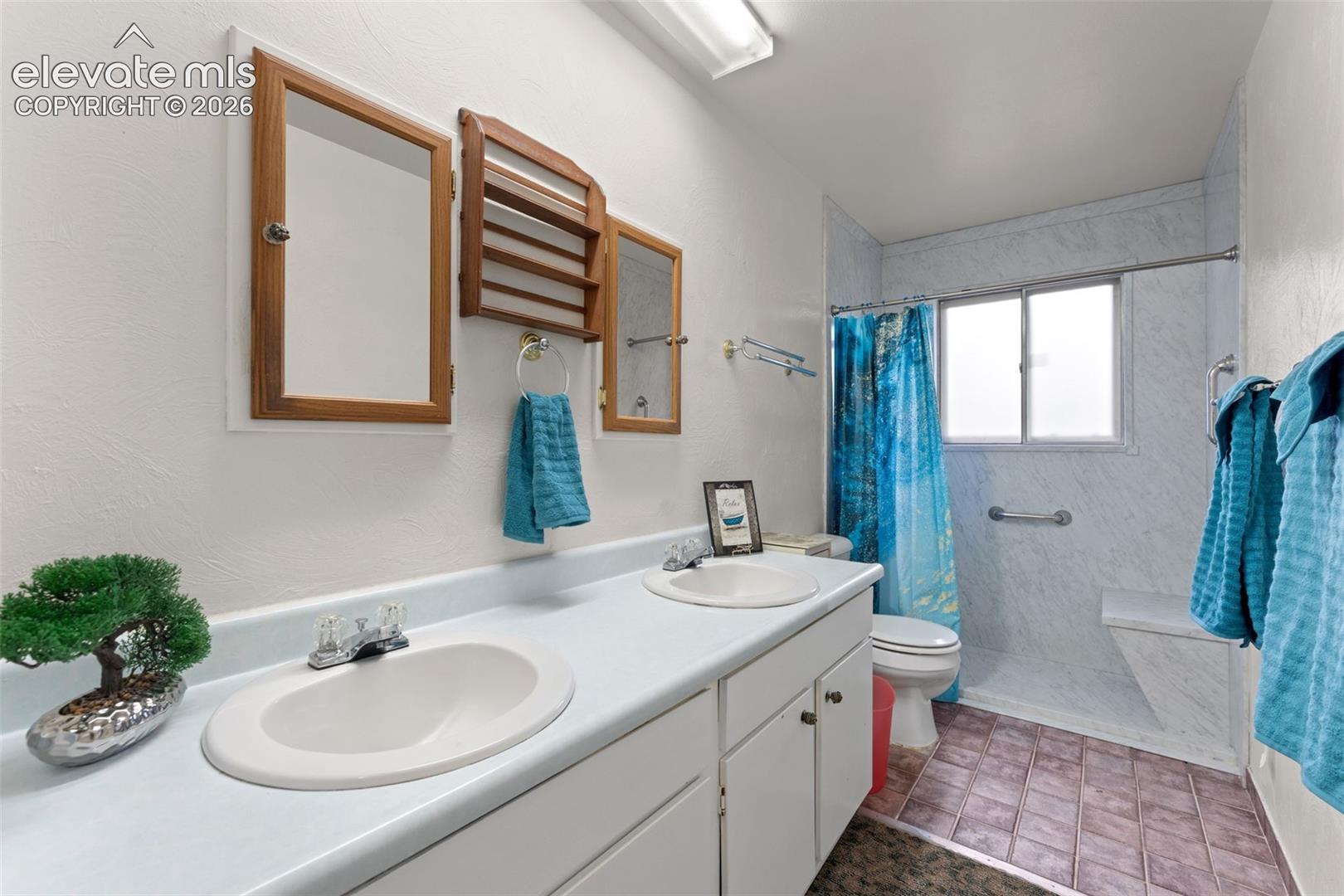 Dual basin vanity with white cabinetry, wood-framed mirrors, and a translucent window