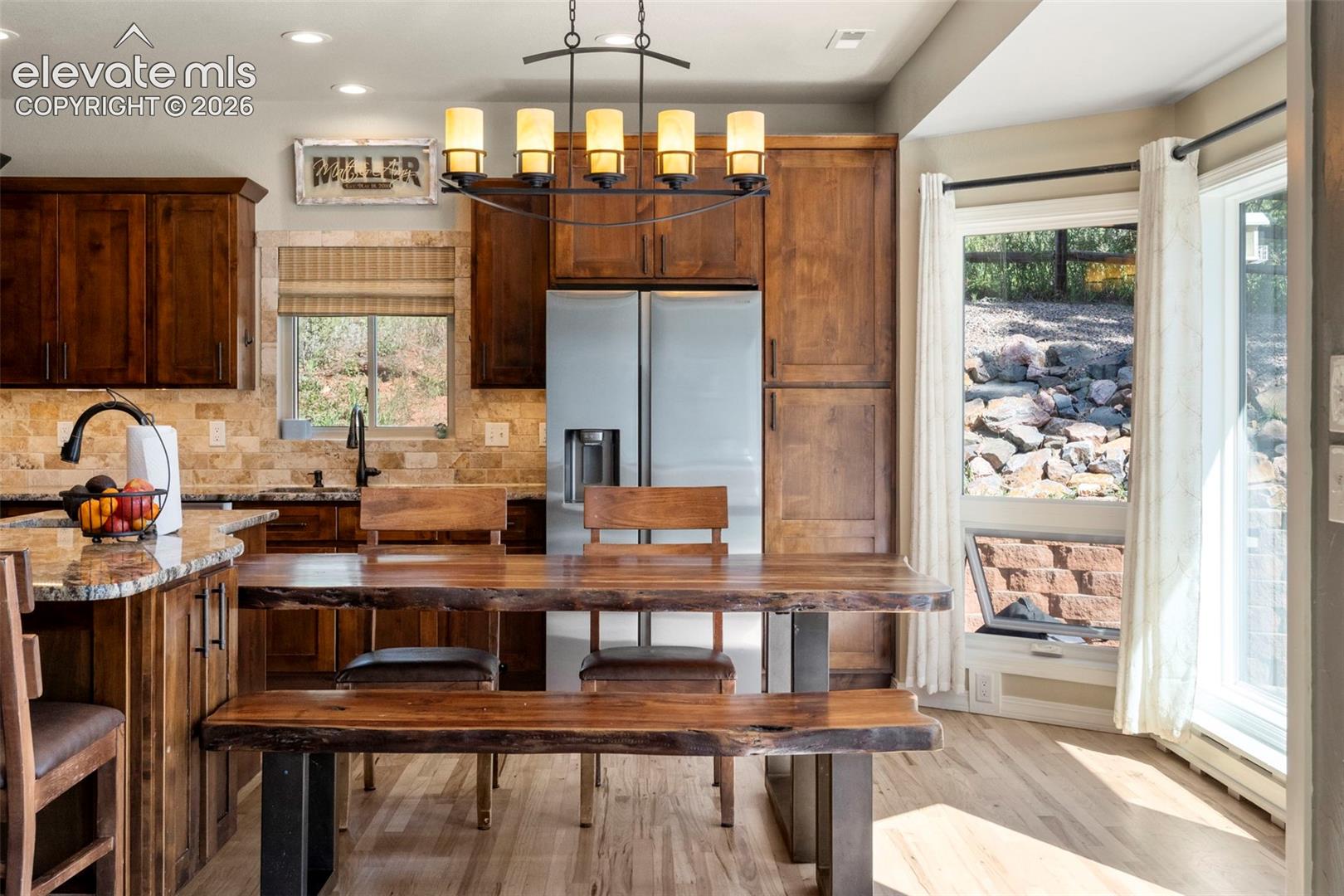 Kitchen with light stone counters, light wood-style floors, stainless steel refrigerator with ice dispenser, backsplash, and pendant lighting