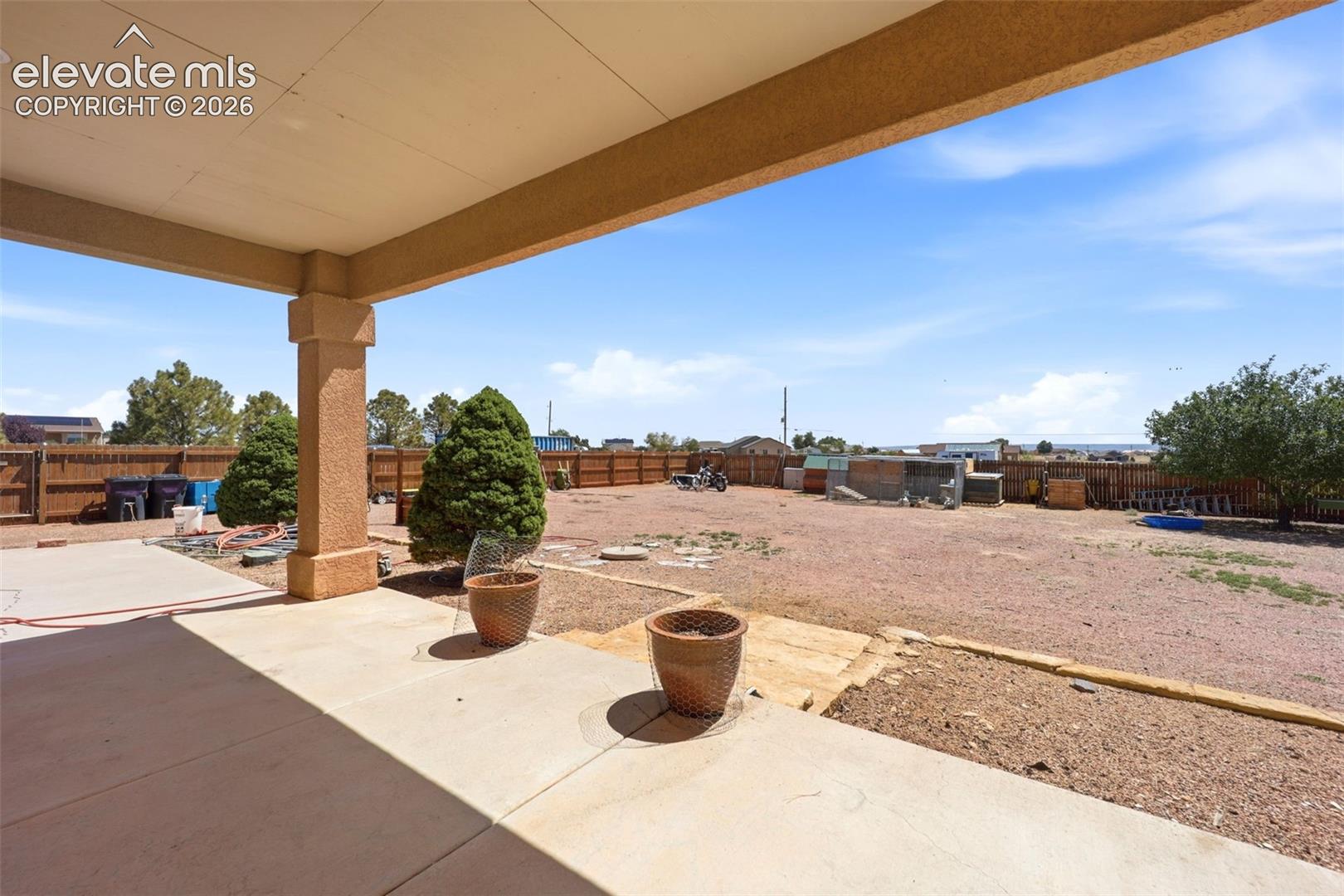 Covered patio with a concrete slab, supporting column, and expansive open yard beyond