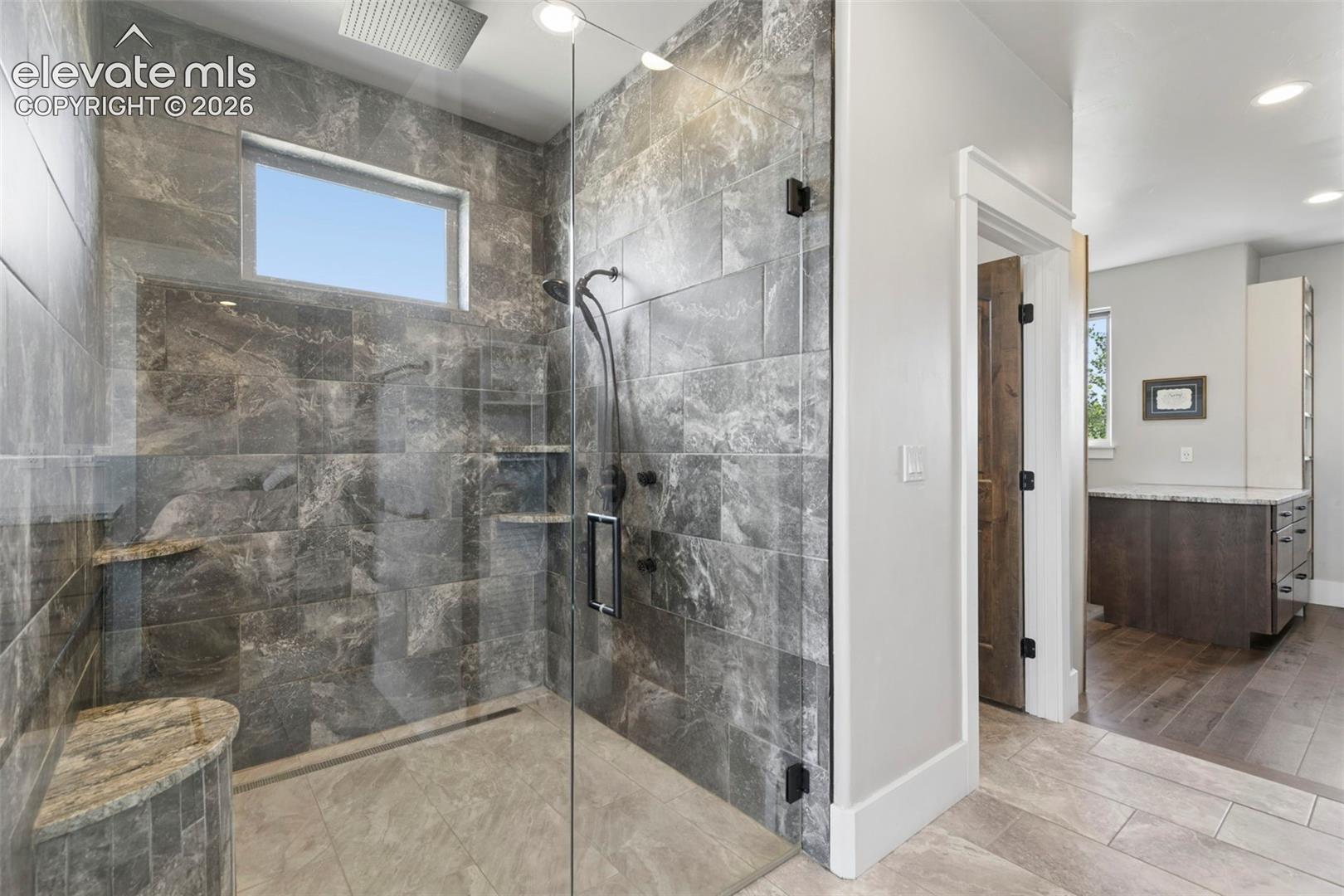 Glass-enclosed shower with full tile surround, integrated shower bench, and recessed wall niches