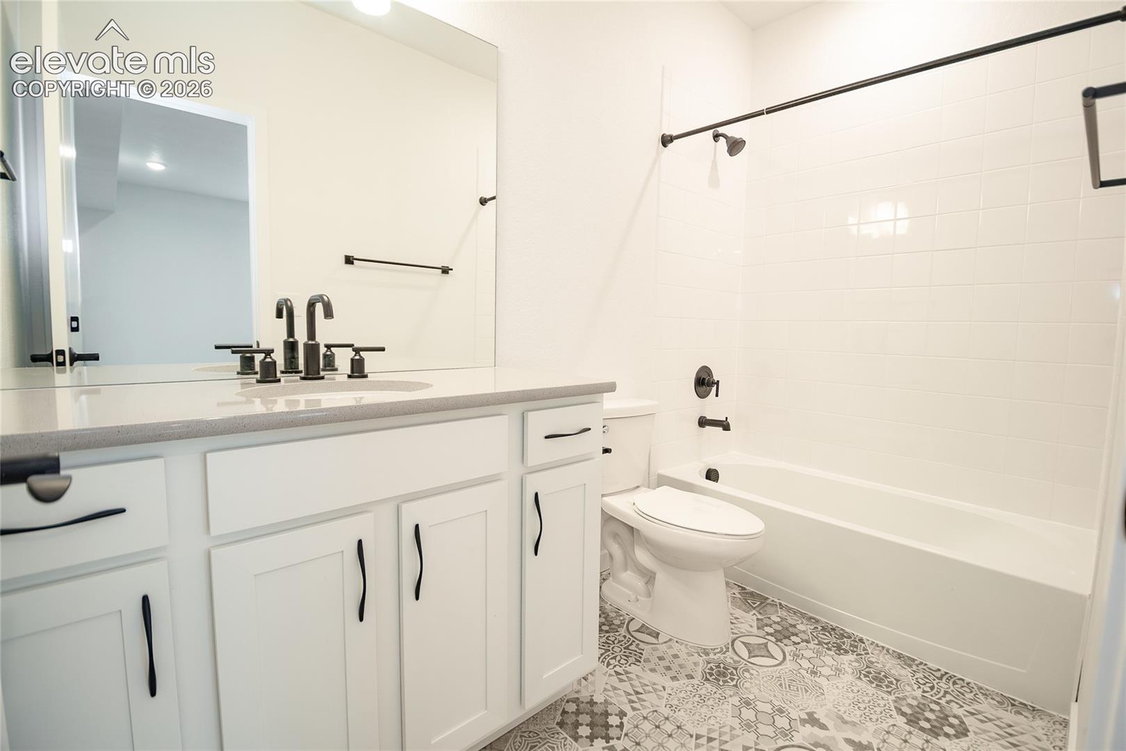White vanity featuring a solid surface countertop, matte black hardware, patterned tile flooring, a large wall-mounted mirror, and a shower-tub combination with matte black fixtures