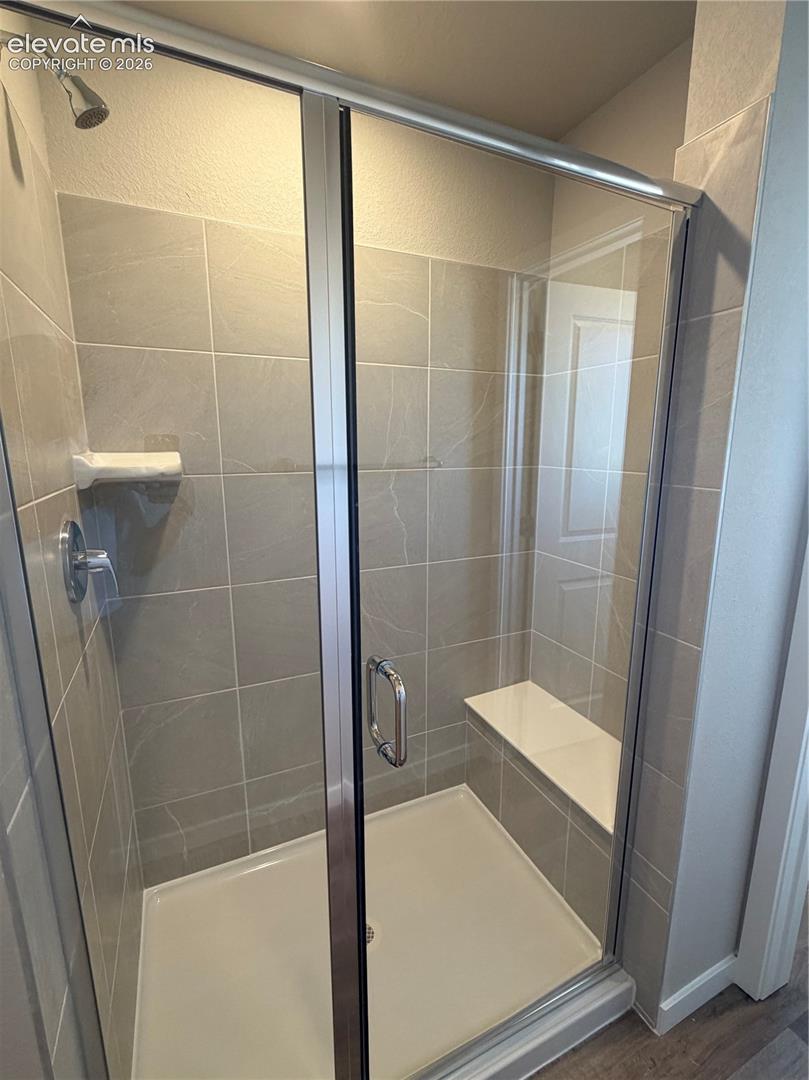 Walk-in shower featuring large-format neutral tile, a built-in bench, a chrome fixed shower head, and a glass door enclosure