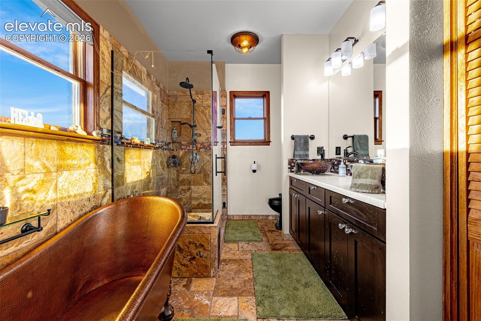 Freestanding copper bathtub, walk-in shower with glass enclosure, dual vanity with vessel sinks, and stone tile flooring