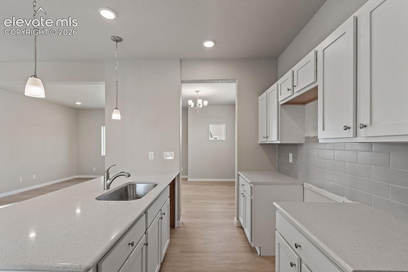 kitchen with white cabinets, quartz counters, undermount sink and pendant lights opening to a living area