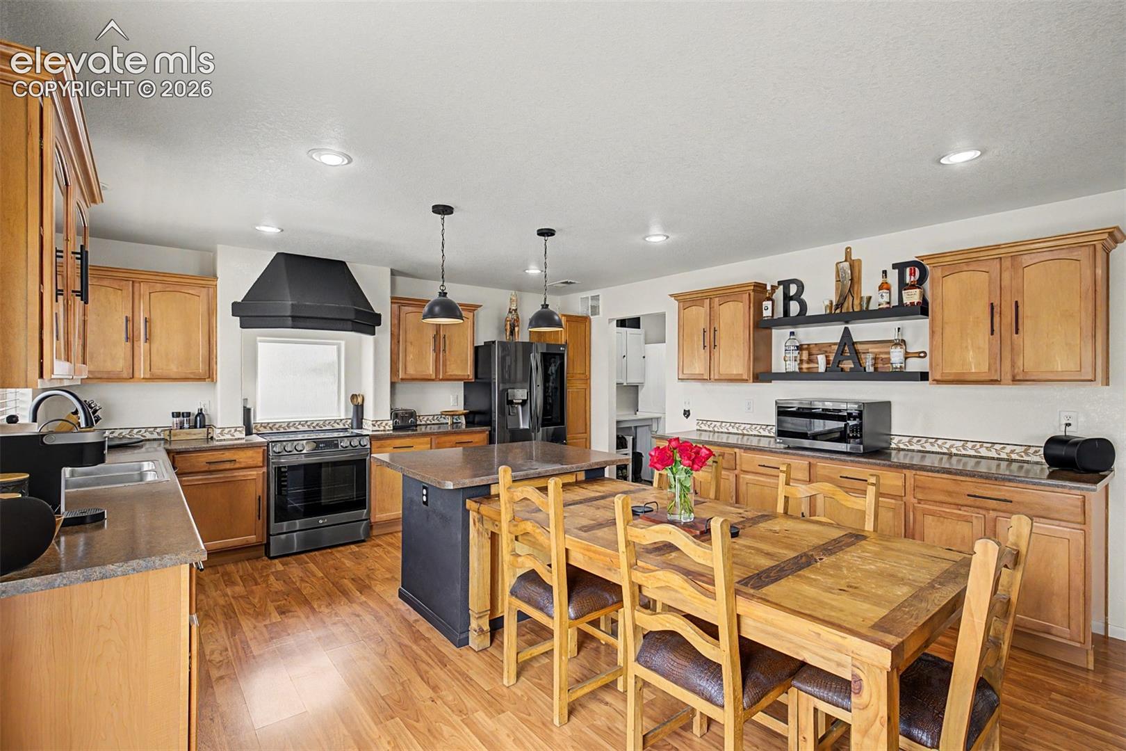 A sleek center island with dual pendant lighting sits at the center of this well-appointed kitchen, flanked by a slide-in range beneath a bold hood and stainless appliances throughout.