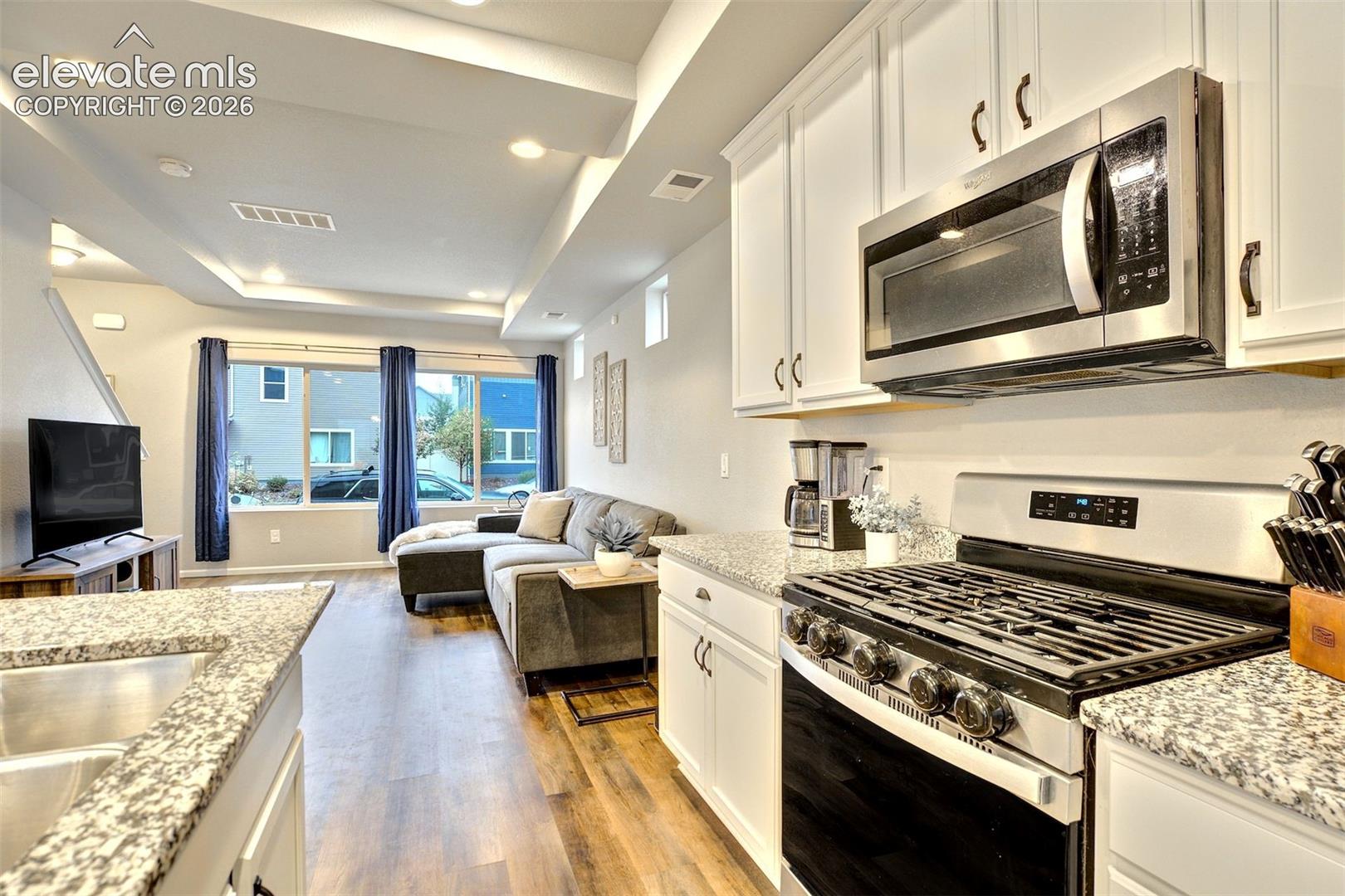 Kitchen featuring white cabinetry, stone-finish countertops, and stainless steel appliances, including a gas range and built-in microwave, complemented by wood-finish flooring and recessed ceiling lighting