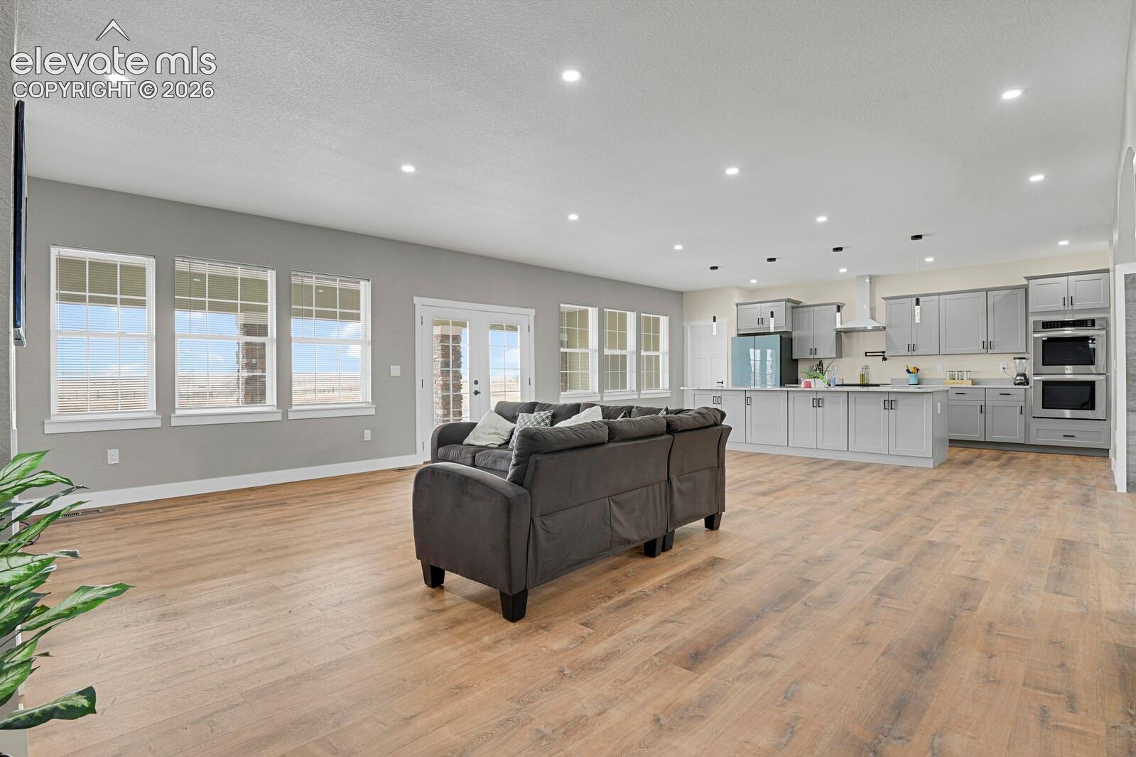 Open-concept living space featuring wood-finish flooring, recessed lighting, a modern kitchen with gray cabinetry, and French doors
