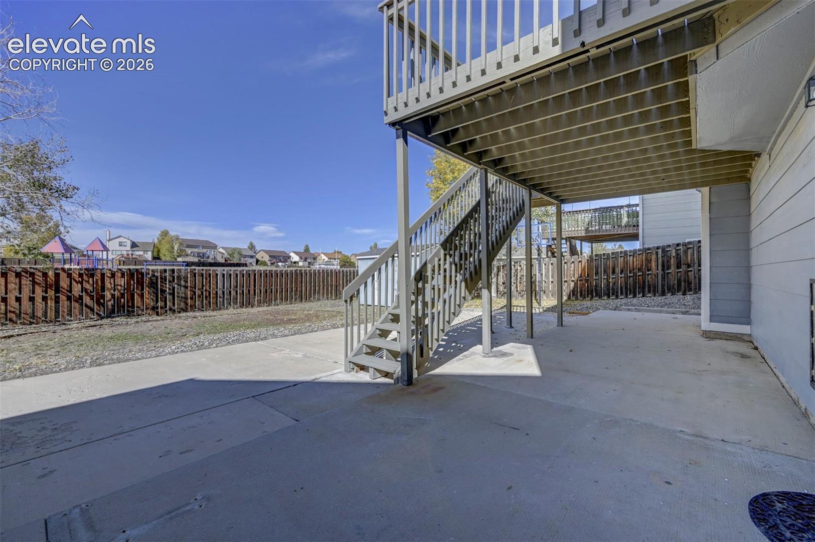 Concrete patio area featuring an elevated wooden deck, exterior staircase, and perimeter wood privacy fencing