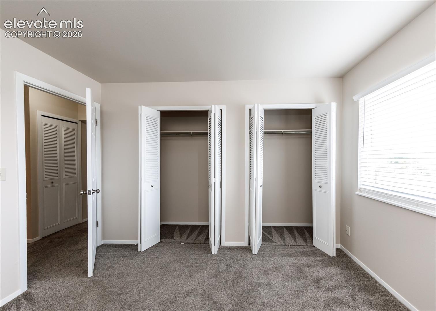 Plush carpeting with neutral wall tones, two bi-fold louvered closets, and a window with horizontal blinds