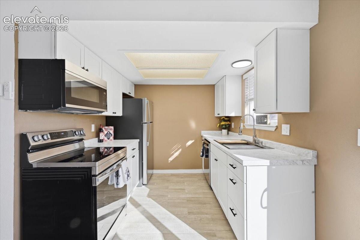 White cabinetry, stainless steel appliances, light-toned wood-finish flooring, white countertops, and a double basin sink