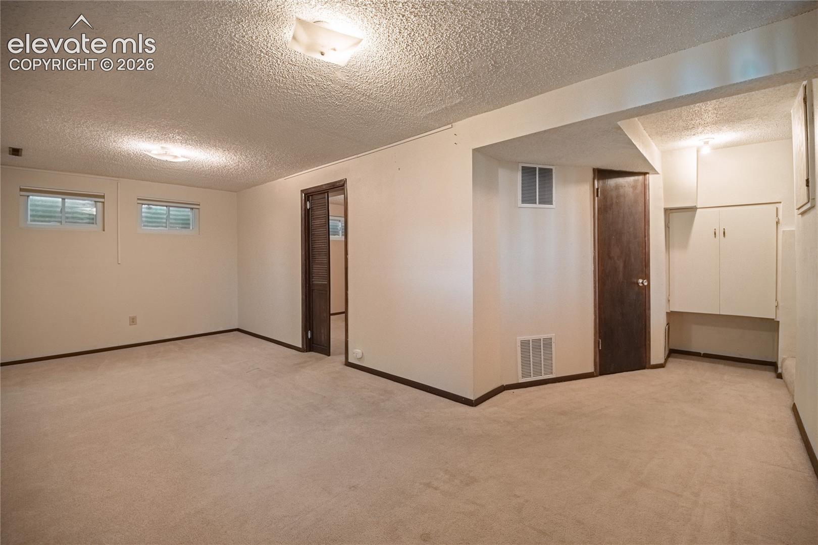 Neutral interior featuring carpeted flooring, two egress-style windows, built-in cabinetry, and interior doors with dark wood finishes