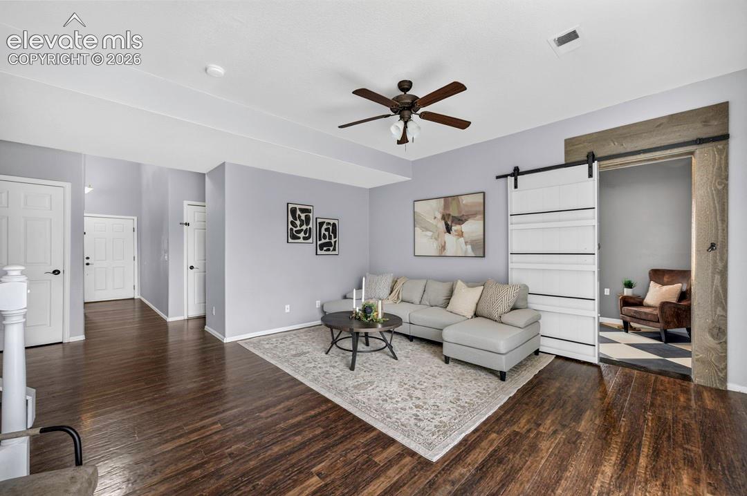Wood-finish flooring, white sliding barn door with dark hardware, rustic wood door frame, and ceiling fan with integrated lighting