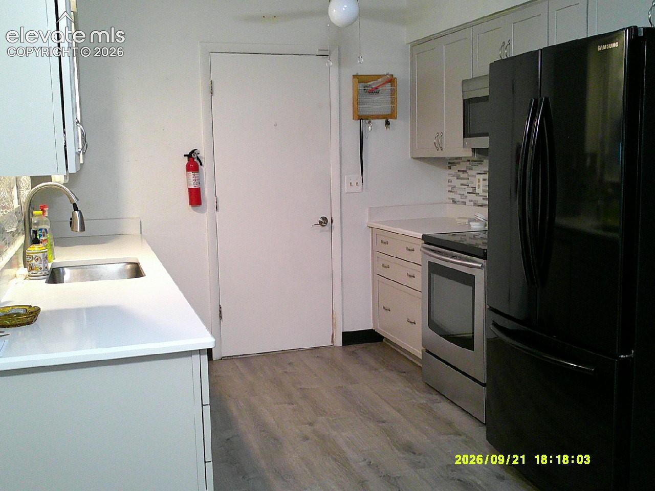 Kitchen featuring light cabinetry, white countertops, a stainless steel sink with a gooseneck faucet, a tile backsplash, and wood-finish flooring