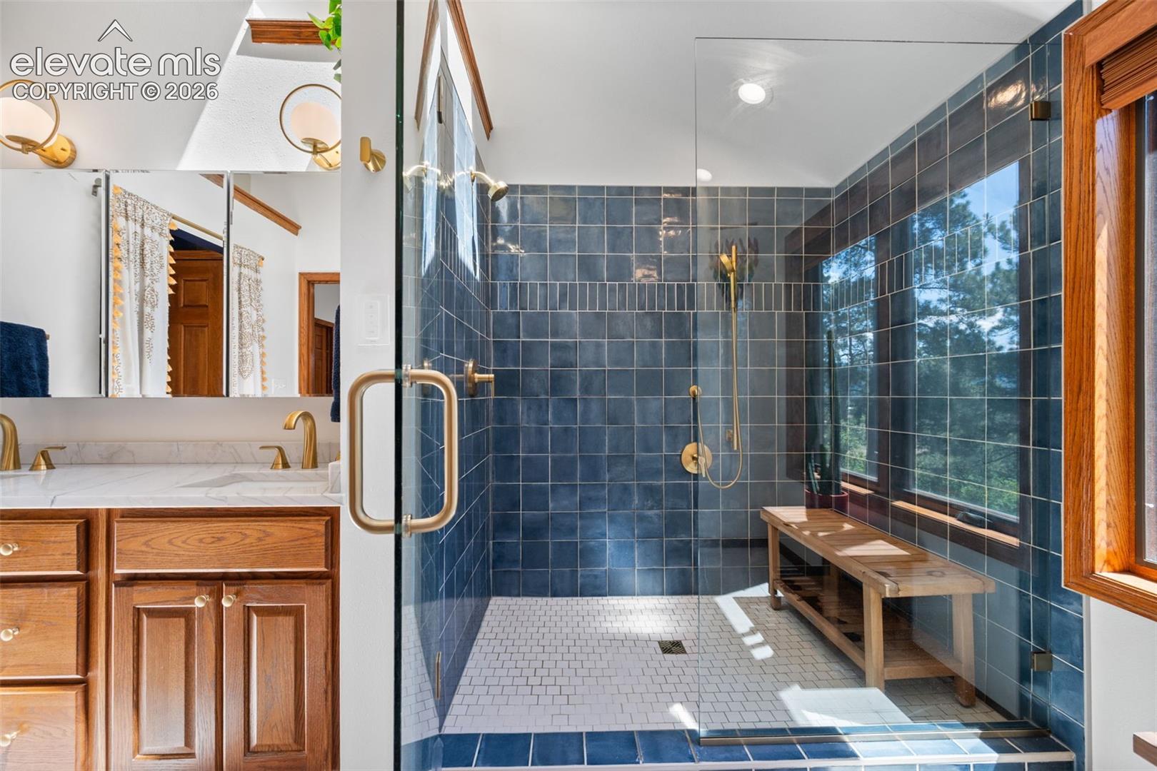 Spacious glass-enclosed shower with blue subway tile surround, white mosaic tile flooring, and a built-in wood bench
