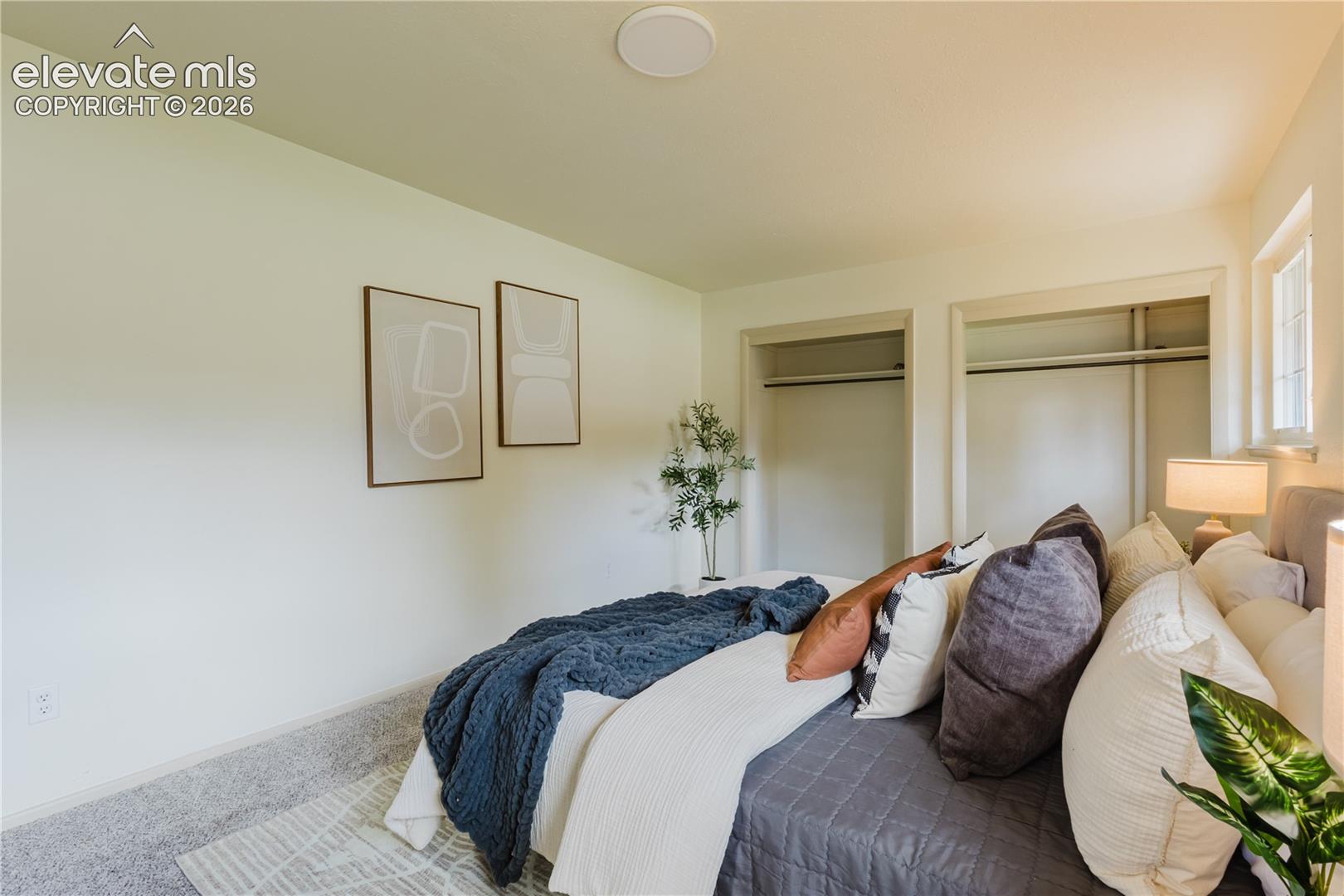 Carpeted bedroom featuring two open closets with hanging rods, recessed ceiling lighting, and a window providing natural illumination