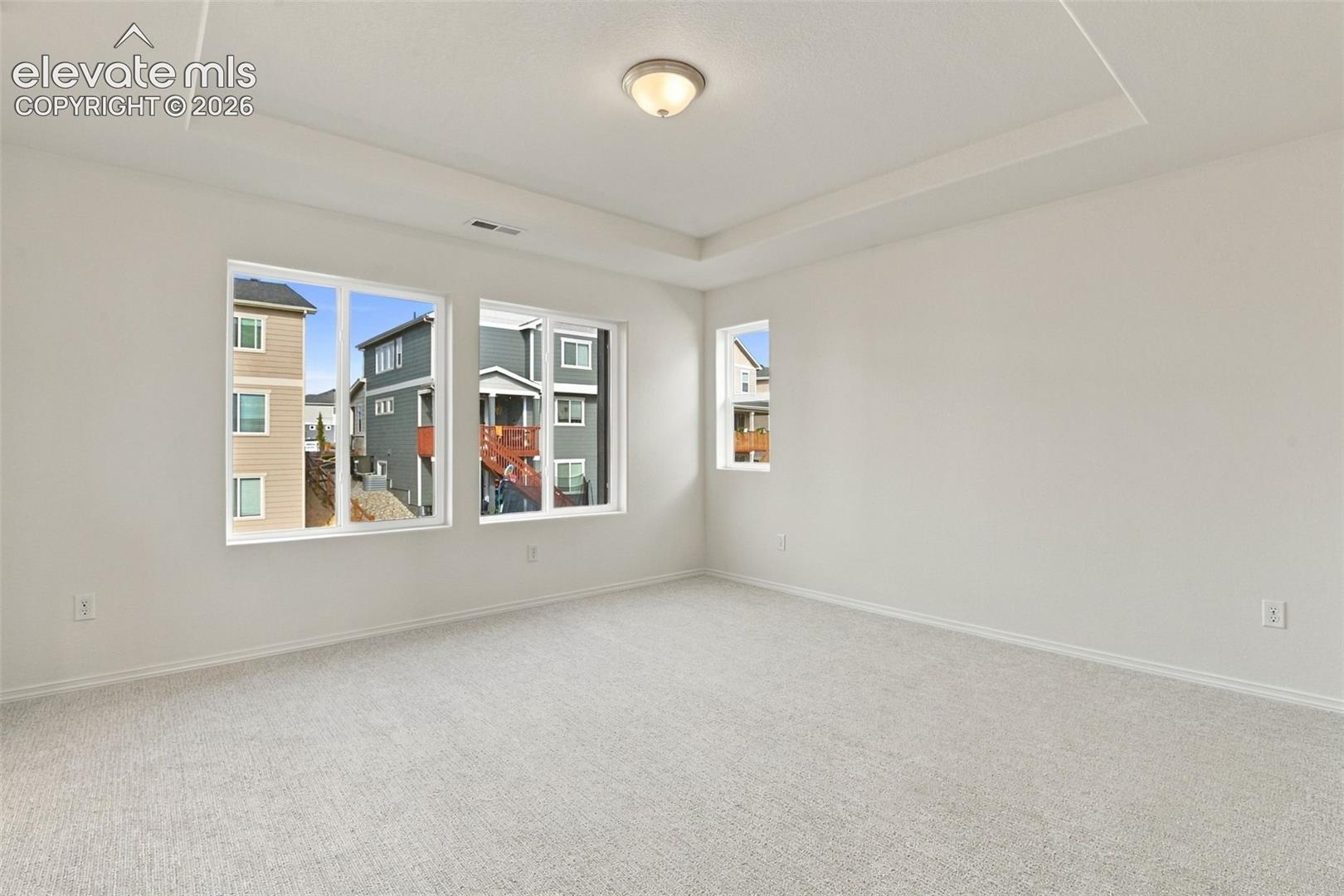 Interior room featuring a tray ceiling, neutral wall-to-wall carpeting, multiple windows, and a central flush-mount ceiling light fixture