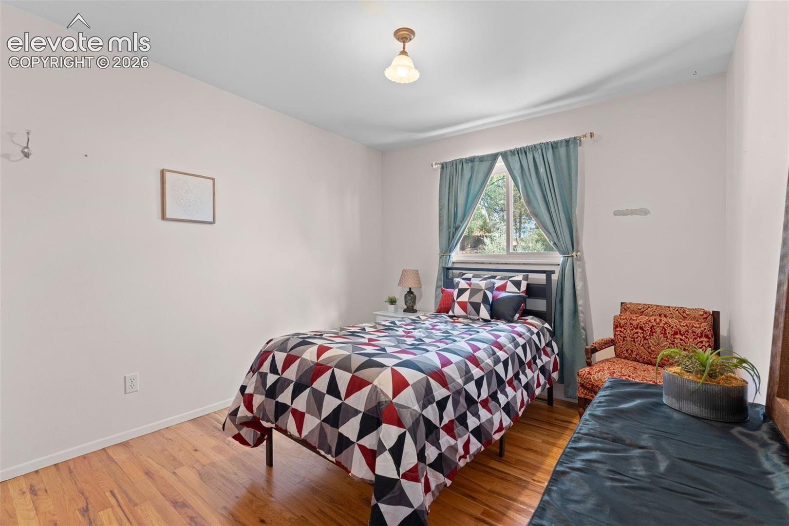 Hardwood-finish flooring, recessed window with light-filtering drapes, ceiling-mounted light fixture, and neutral wall tones