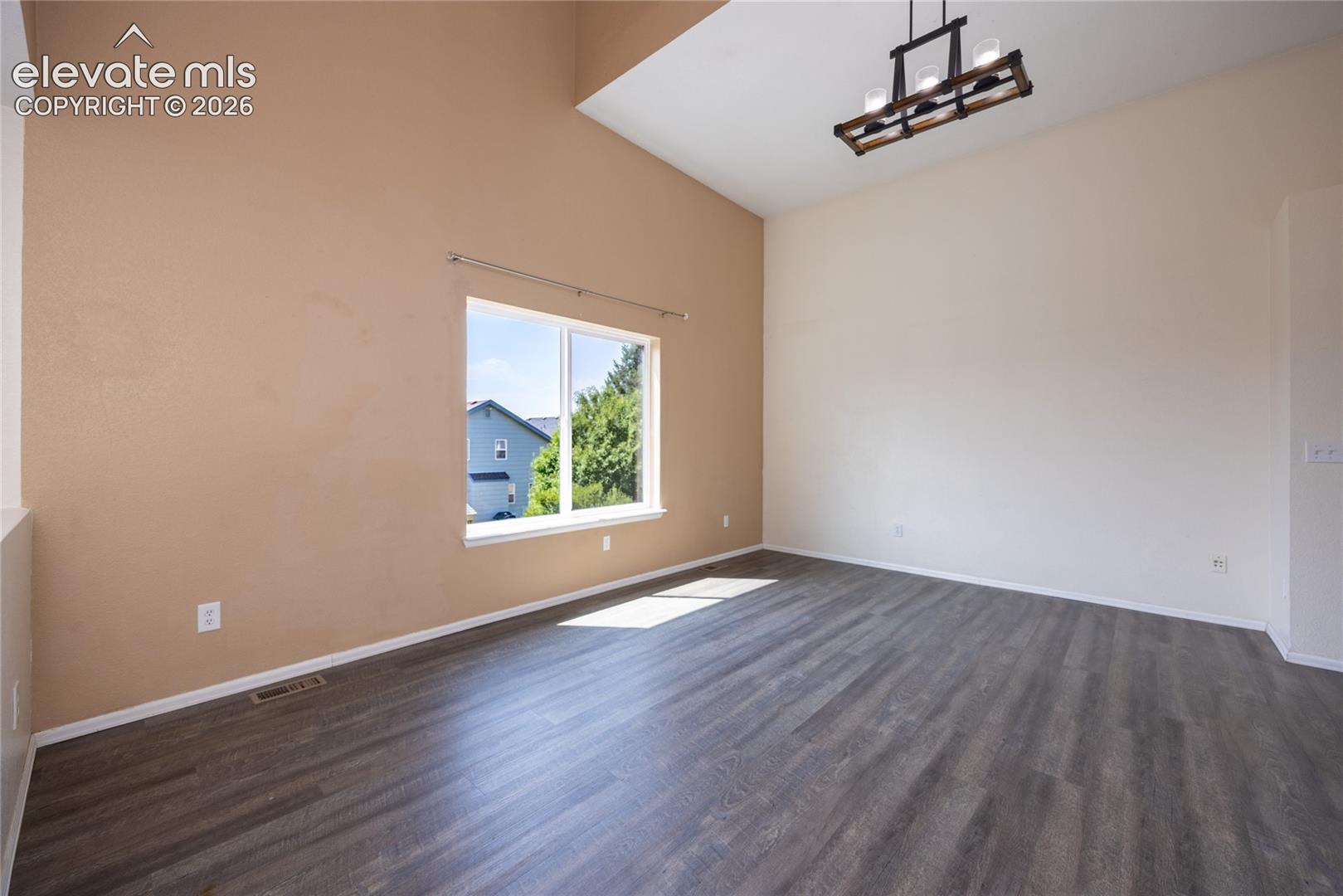 Vaulted ceilings with a decorative chandelier, wood-finish flooring, and a large window
